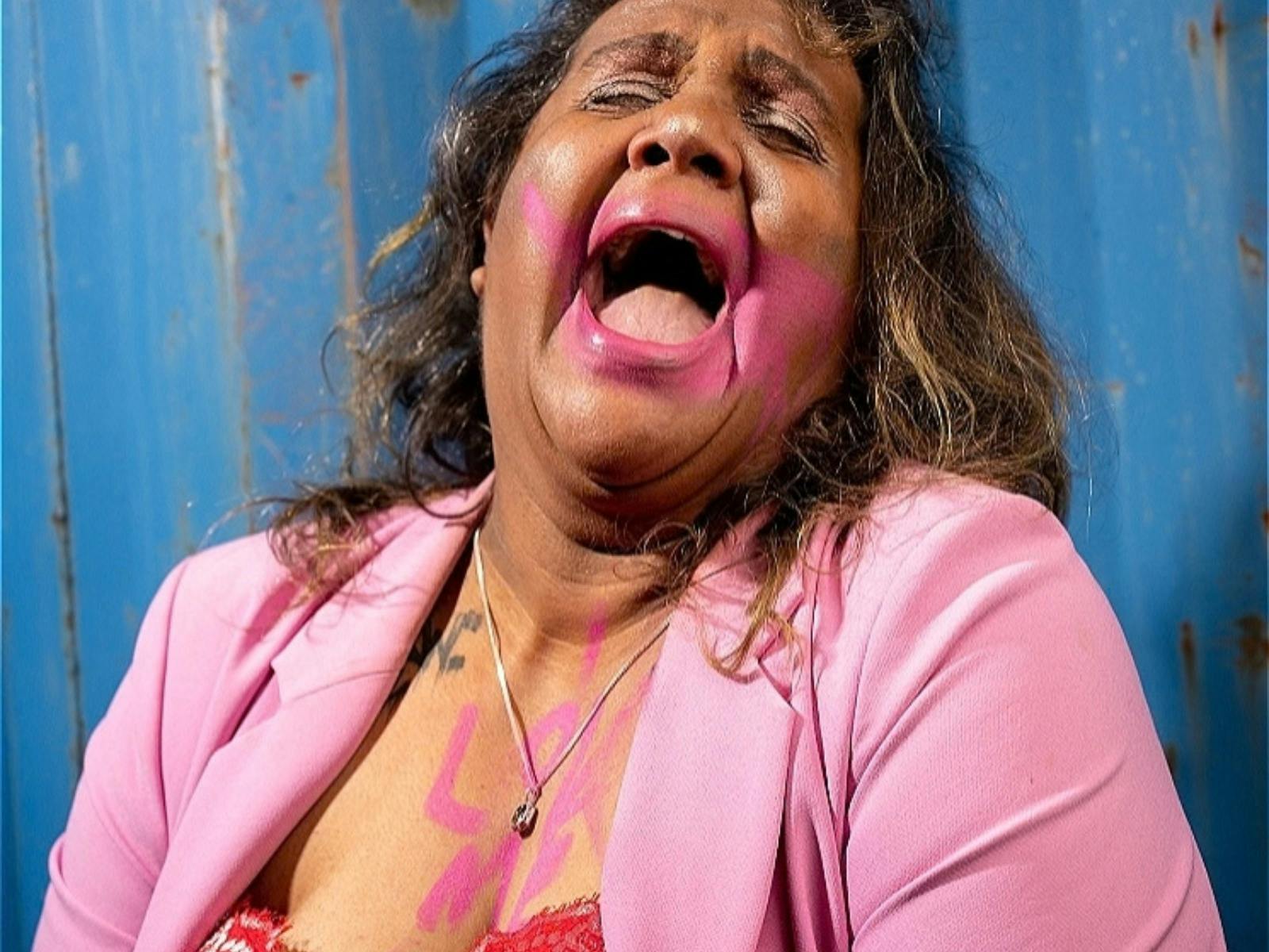 A First Nations woman in a pink blazer with makeup smeared and looking to be crying