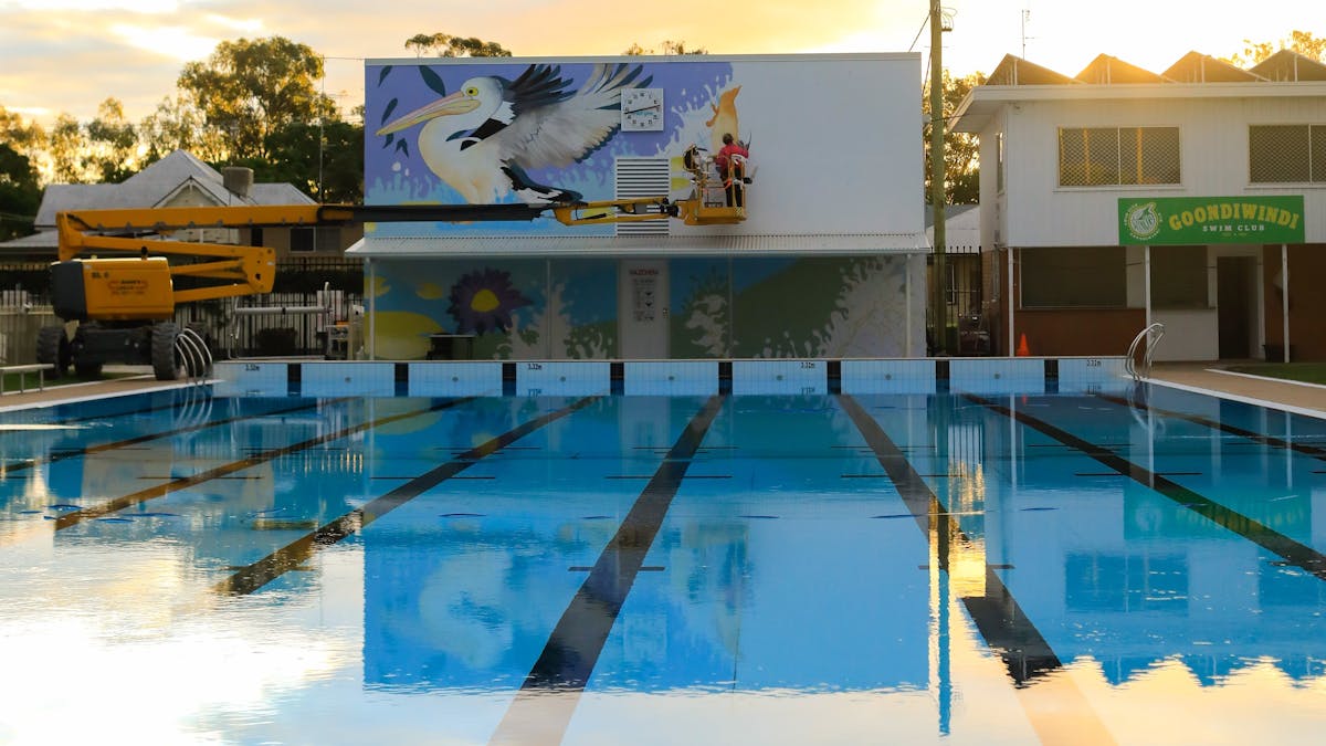 Tia Carrigan on a scissor lift painting a mural on a  wall at the Goondiwindi Pool