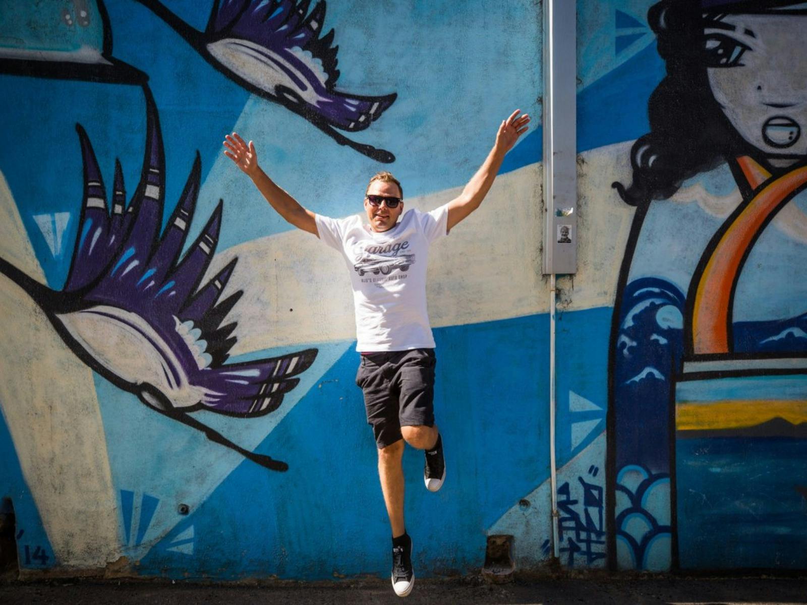 Man standing in front of wall with arms up high with graffiti in back