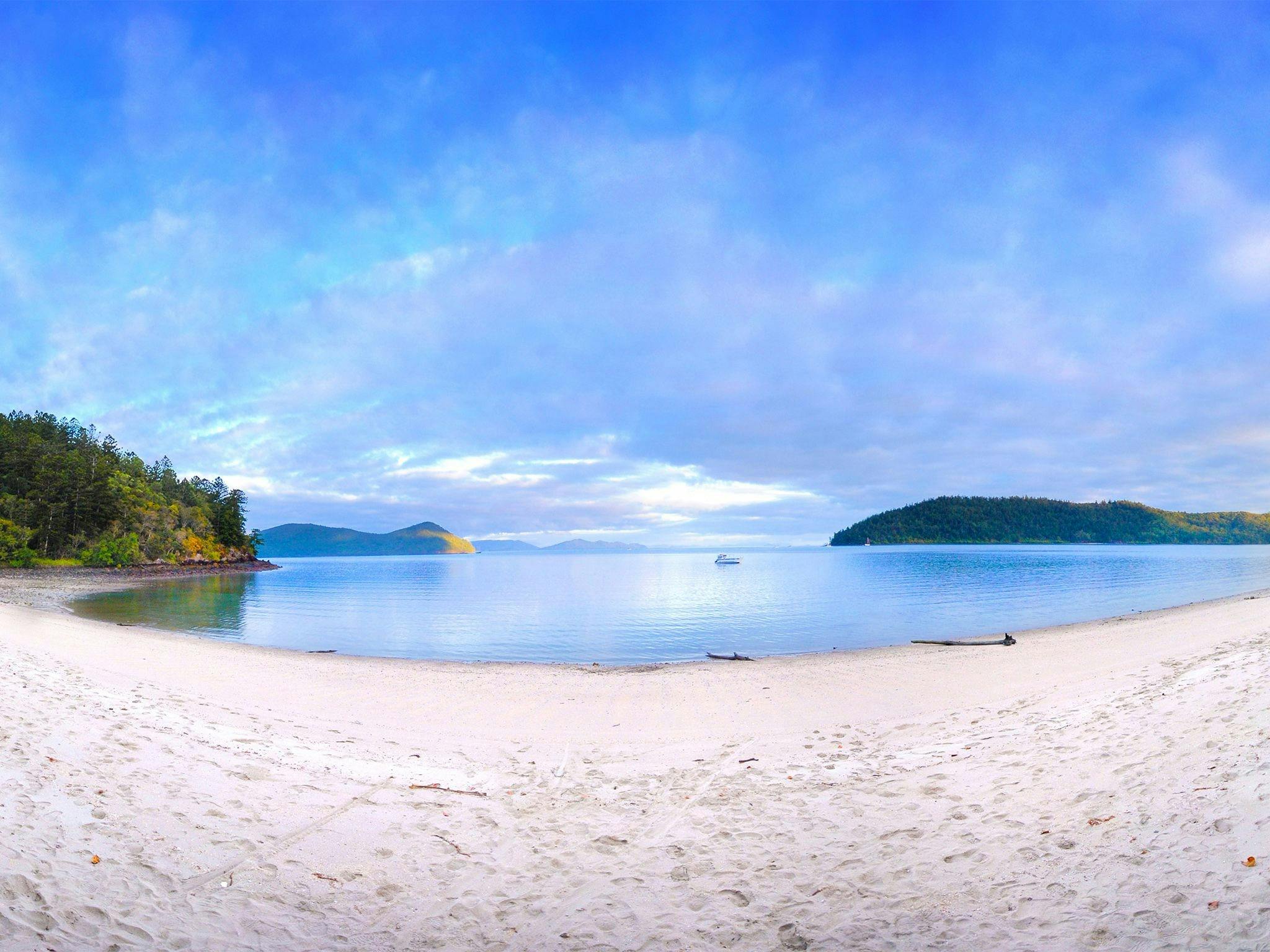 Beach looking out over a bay with islands and a boat in the background.