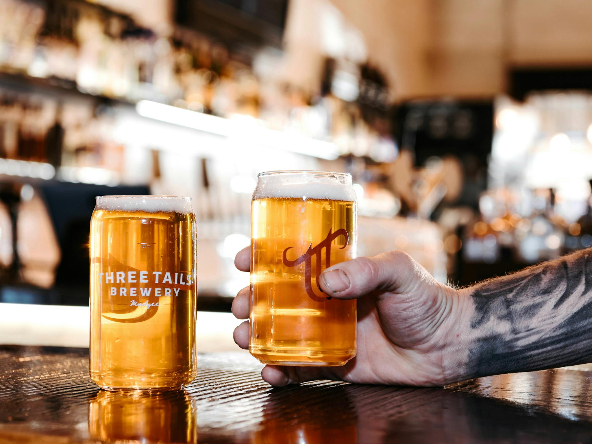 A hand picking up a glass of beer off the bar
