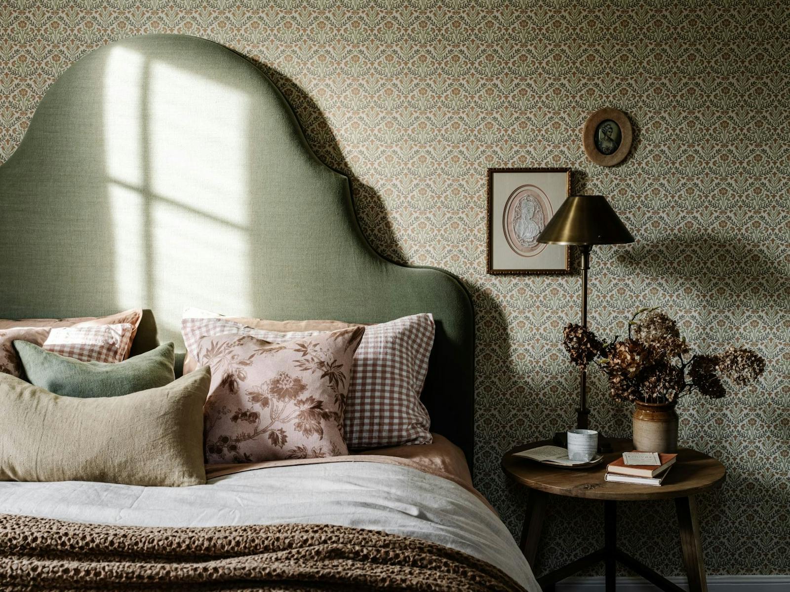 A bedhead and bed drenched in natural light, with luxurious linen and wallpaper.