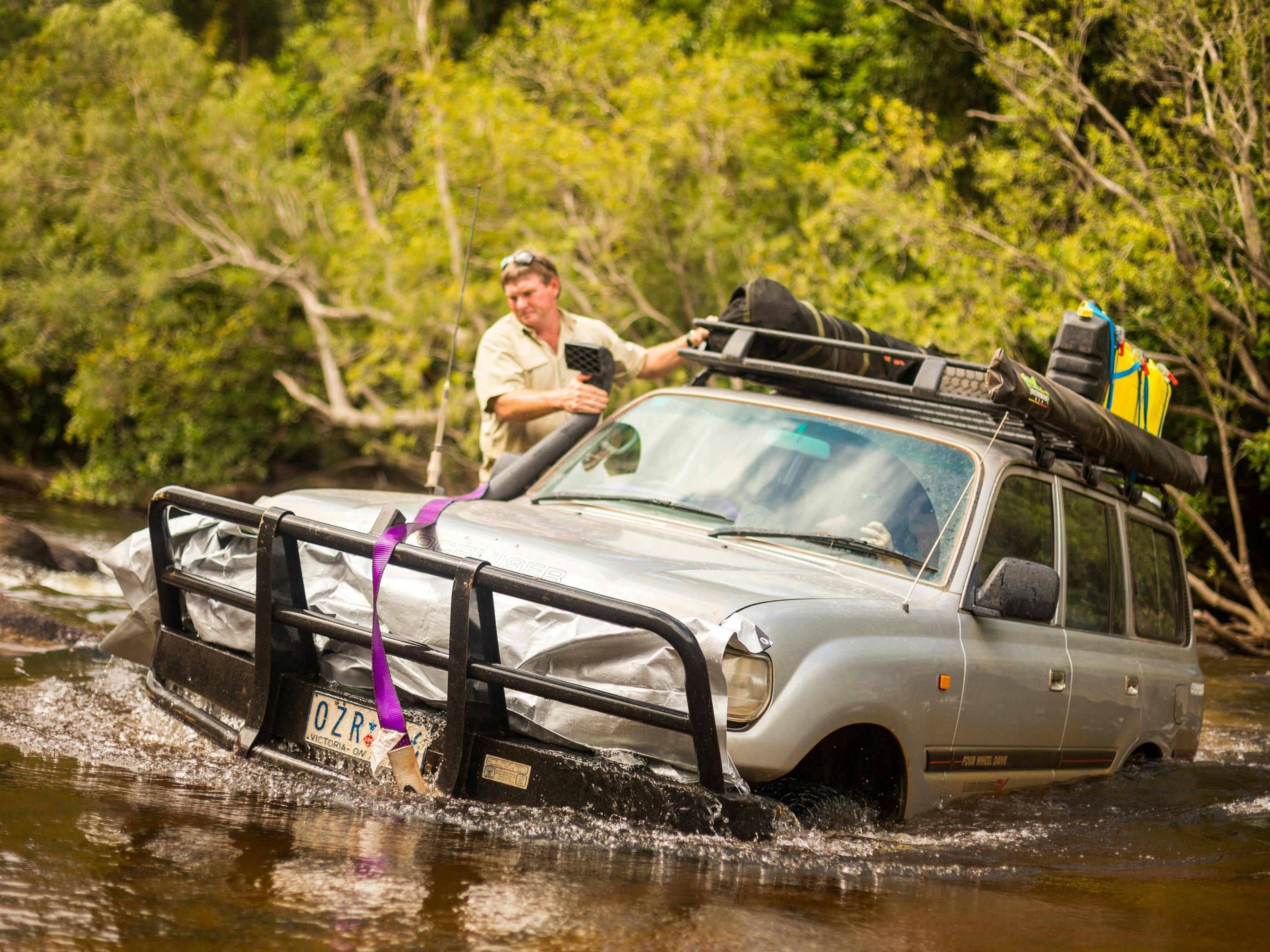 Toyota Landcruiser driving through deep water crossing with guide stood on side step ready to help!