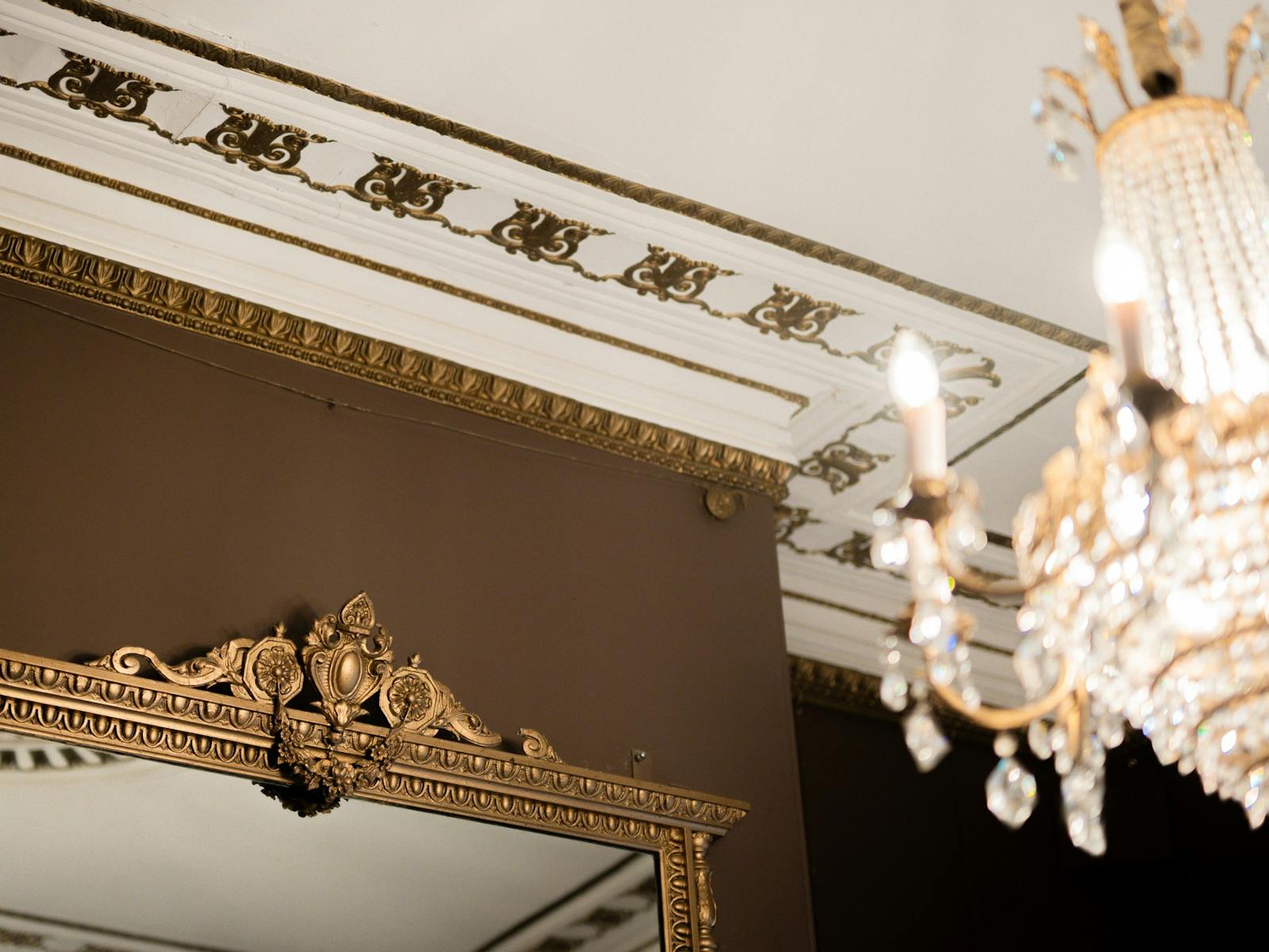 White ceiling with gold gilded cornicing details, and an ornate golf framed mirror on a brown wall