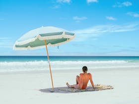 Guest relaxing beneath a beach umbrella on the white sands of the Eyre Peninsula near Port Neill.