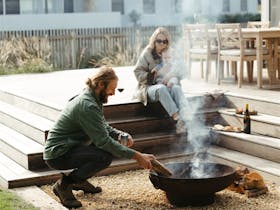 Couple sitting by outdoor fire pit with wine at Tea Tree Retreat accommodation in Robe South Austral