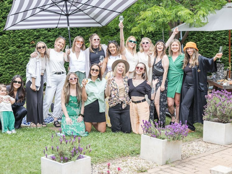 A group of ladies celebrating and drinking champagne in a green leafy courtyard.