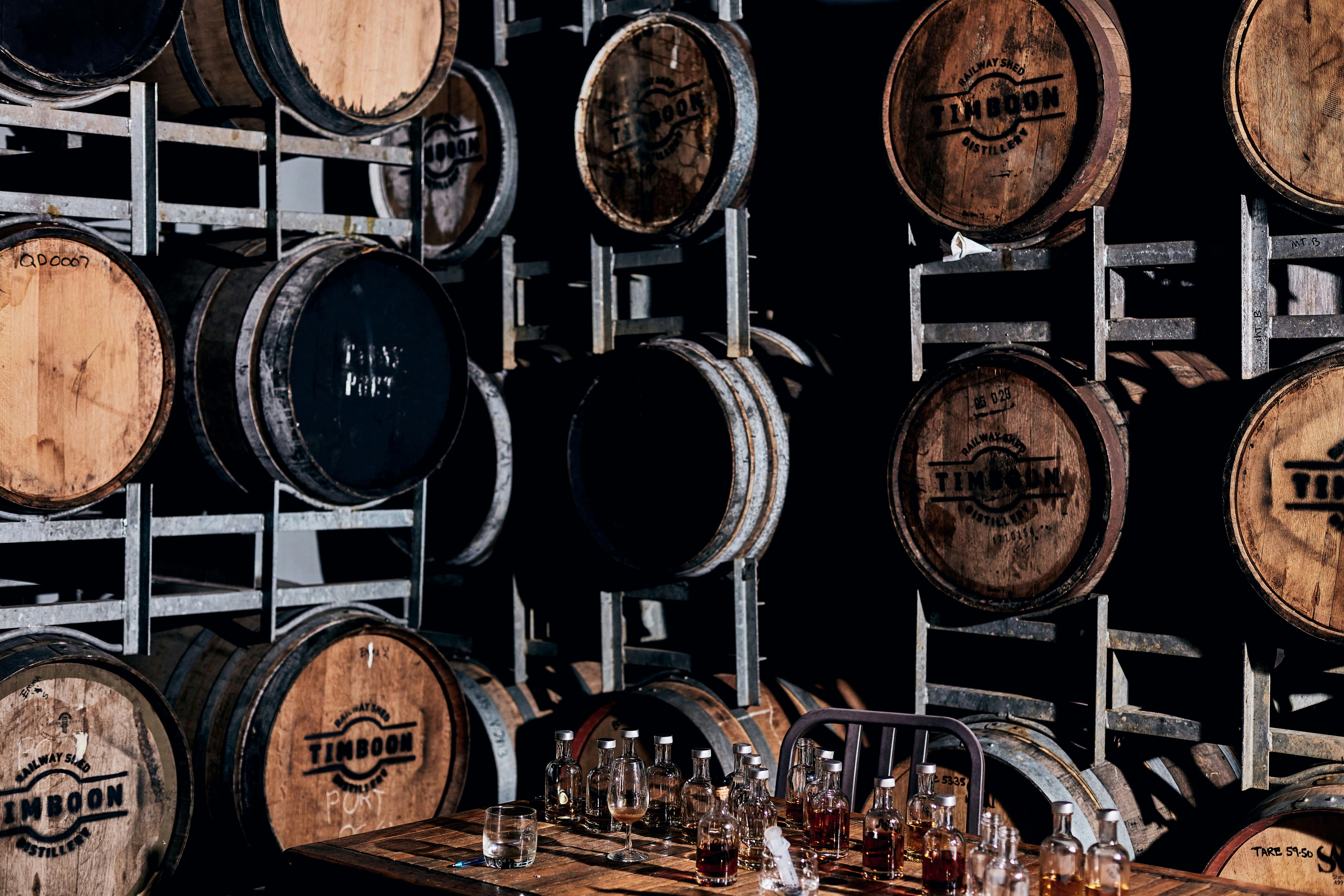 Stacked whisky barrels in a bond store, with a table with whisky tasting bottles on top.
