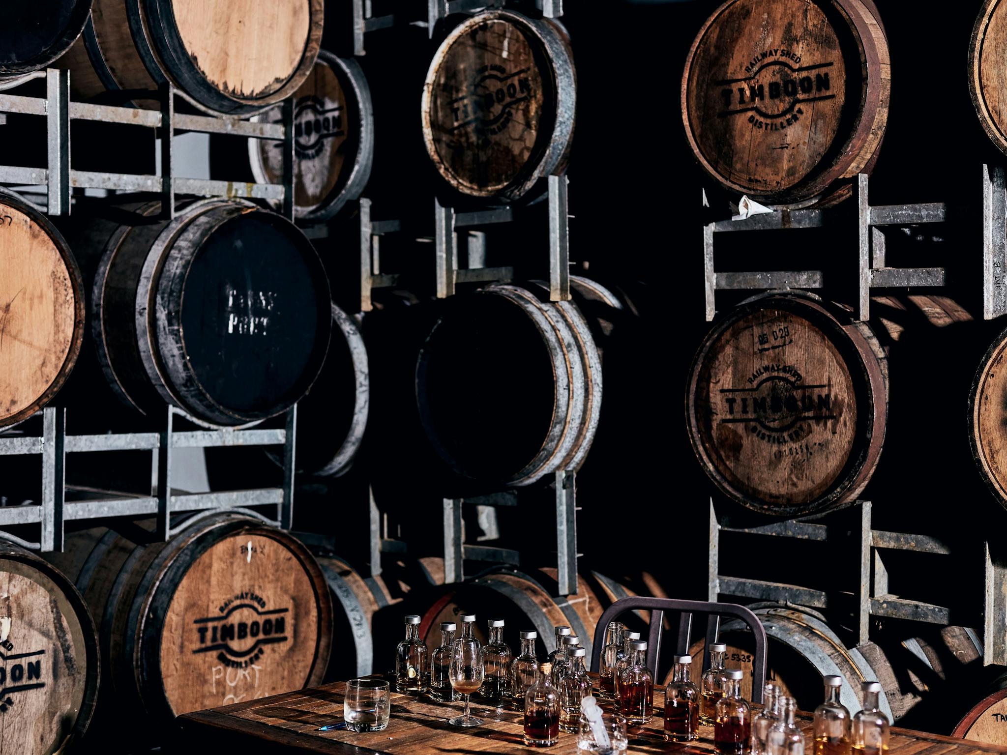 Stacked whisky barrels in a bond store, with a table with whisky tasting bottles on top.