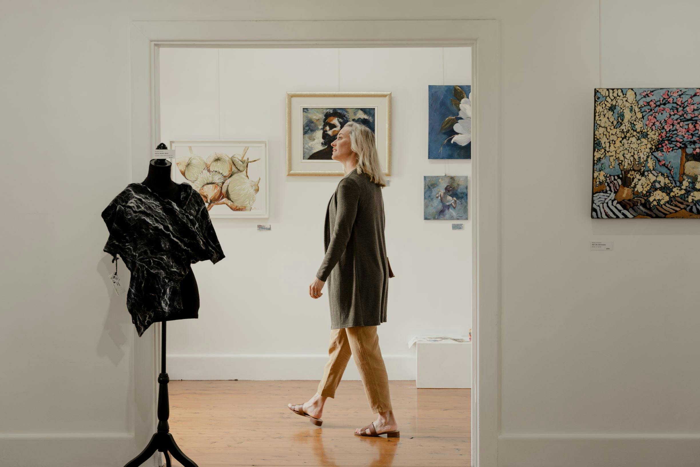 A woman is seen through the doorway of a white art gallery, paintings on the walls around her.