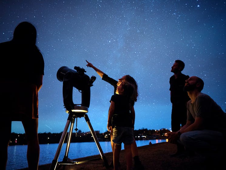Group of people at night outside stargazing next to a telescope