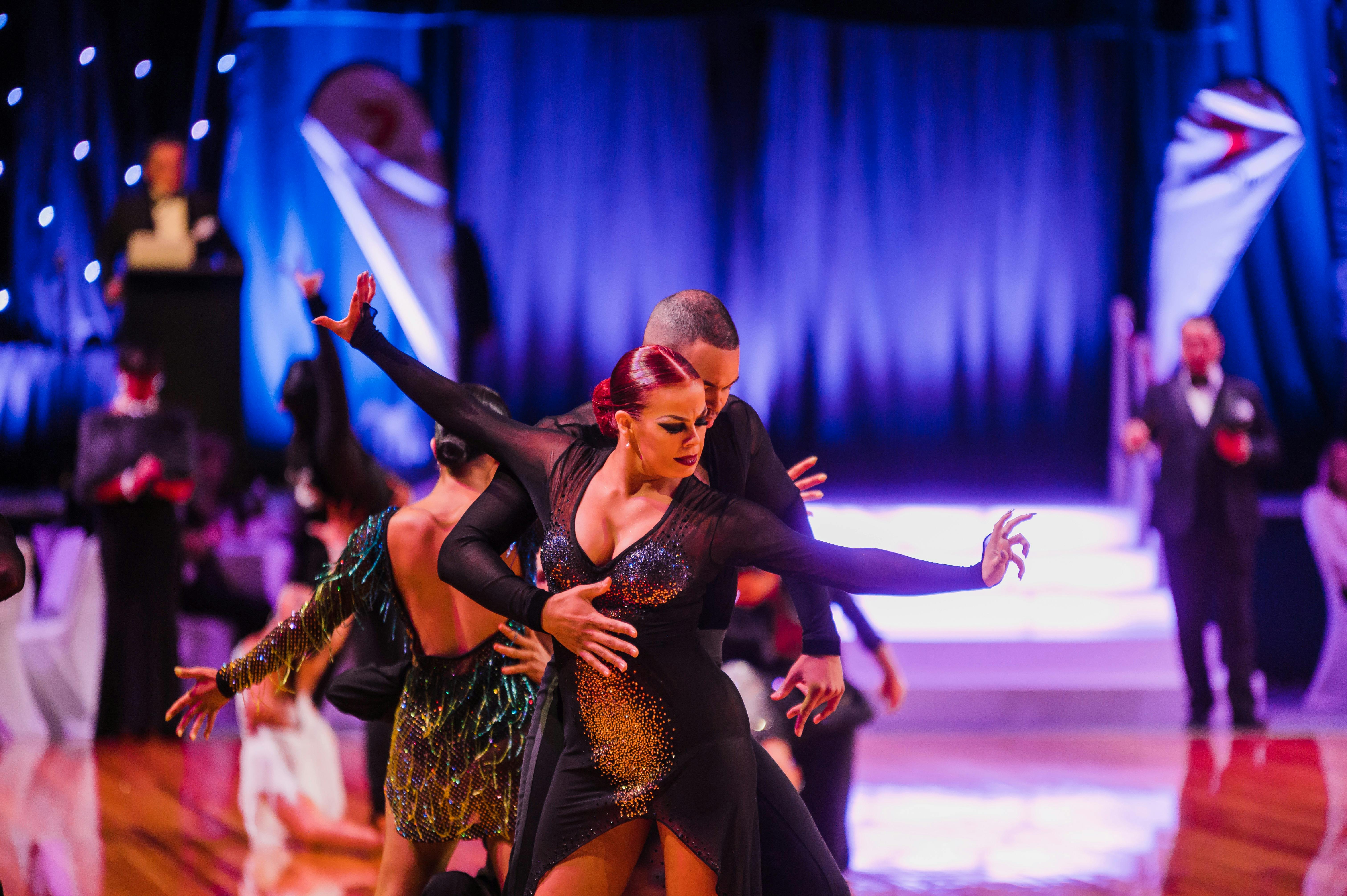 Two dancers peform latin dance on dance floor with adjudictors in the background