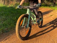 A child rides a green bike on yellow dirt.