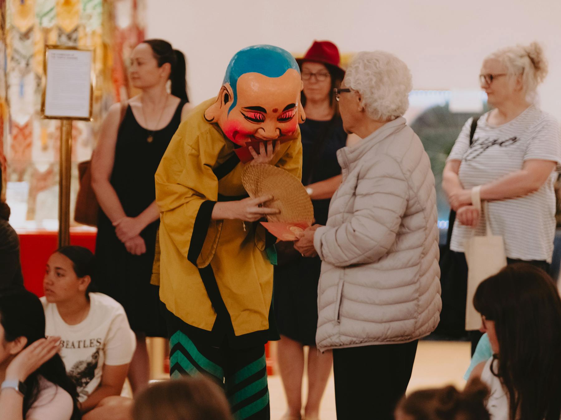 Image of someone in chinese attire and mask accepting offering from a woman in grey jacket