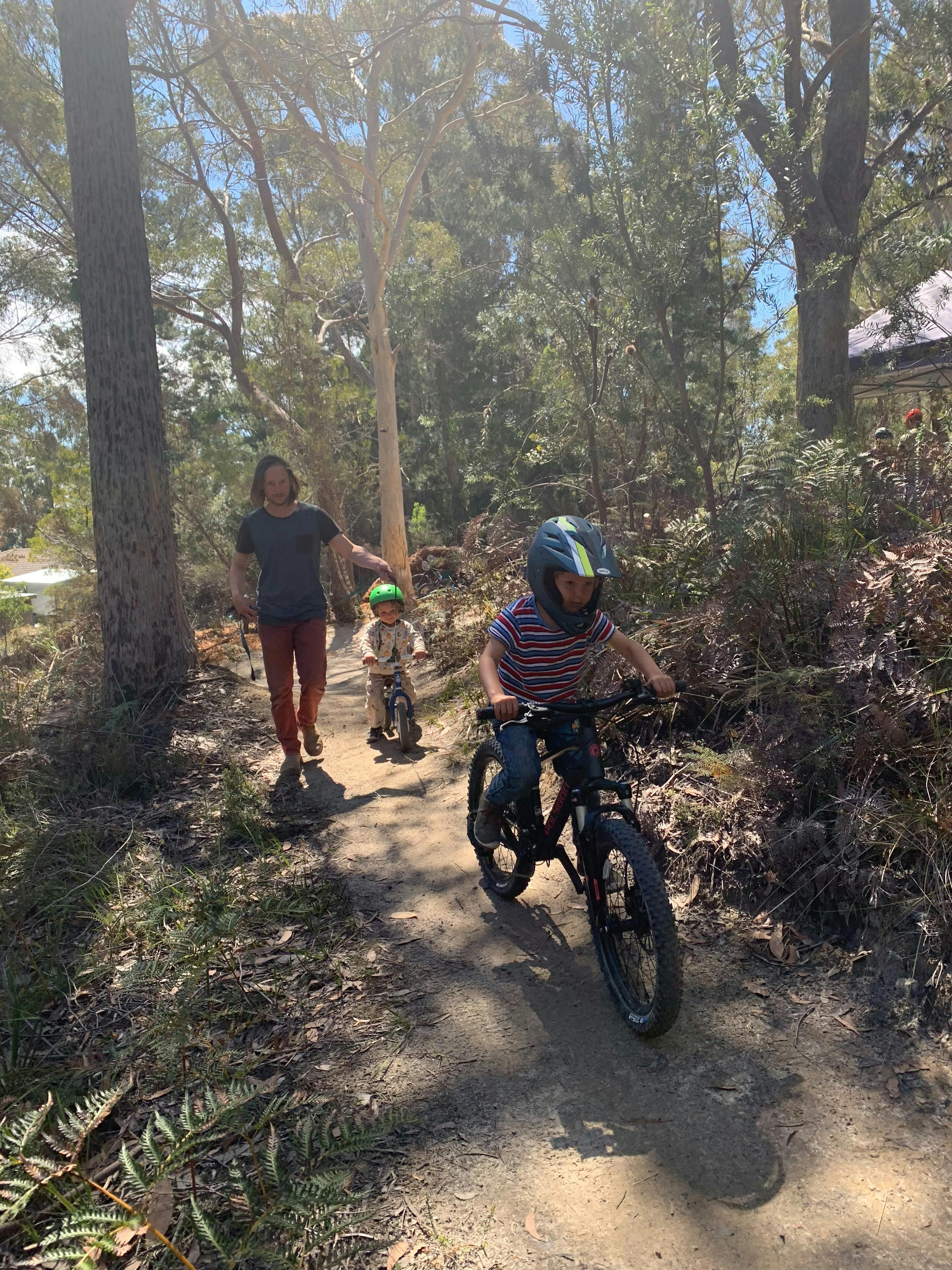 A Dad walks with his sons while they are riding their bikes along a bush track.