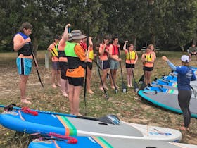 Group of school students having a safety briefing on land before their standup paddleboard session