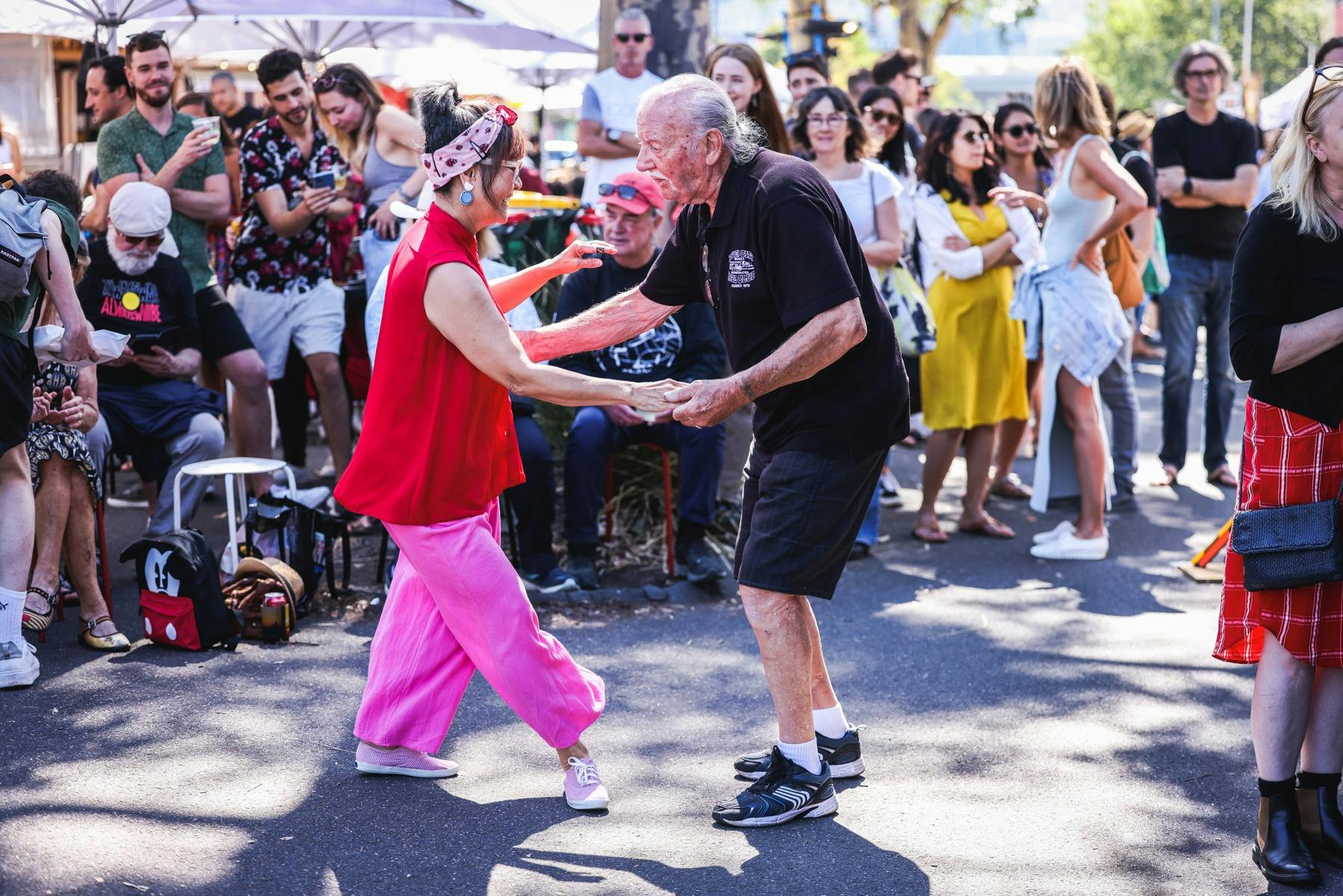 Two people dancing in the middle of a crowded outdoor event, surrounded by onlookers