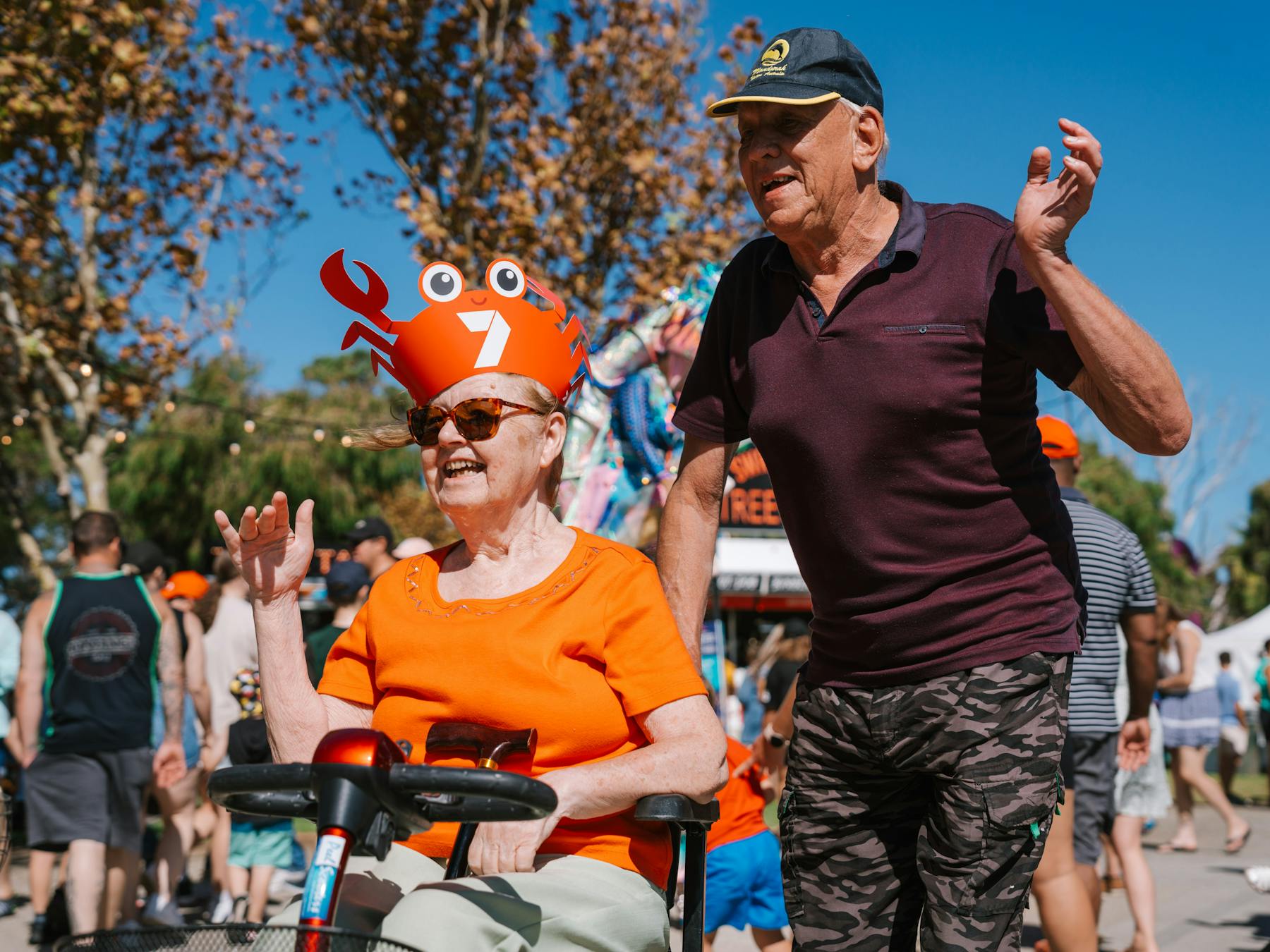 Woman sitting on scooter and man walking next to her smiling and waving