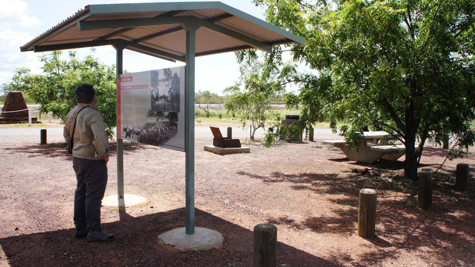 General view of the Attack Creek Memorial roadside stop, with sheltered interpretive signage, camping / picnicking facilities in the background, and the Stuart Highway  beyond.