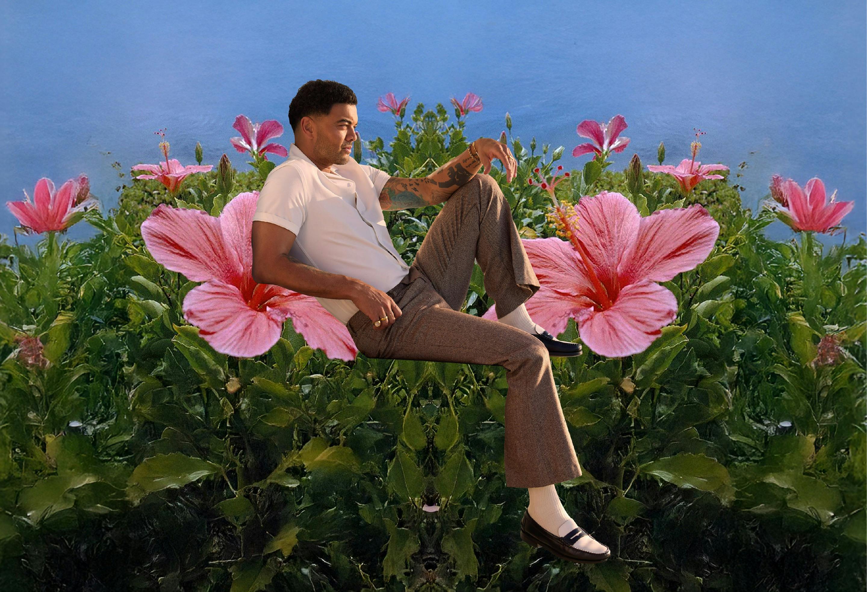 Guy Sebastian posing in front of background of pink flowers.