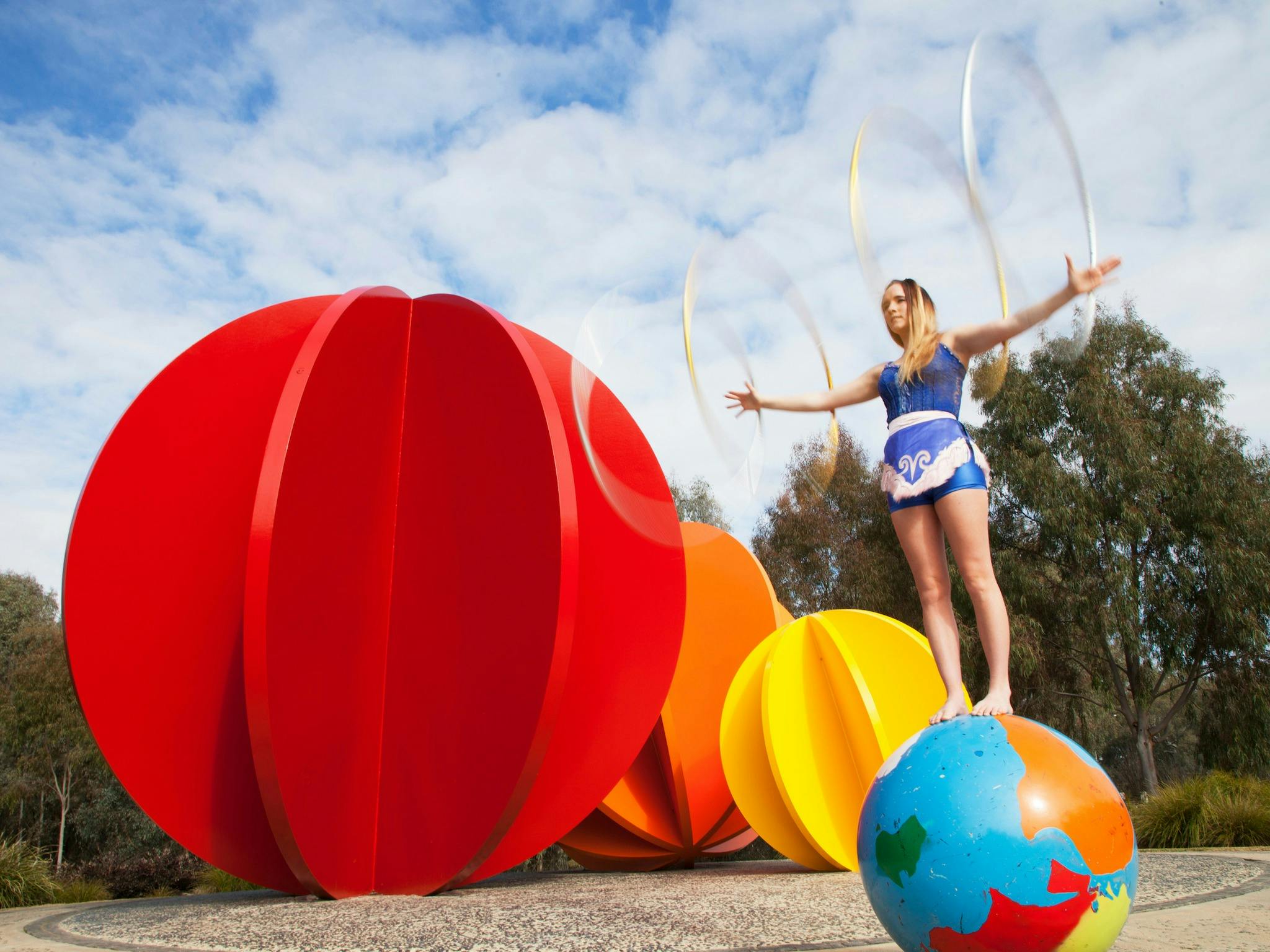 Flying Fruit Fly Circus student balancing on a globe with hula hoops