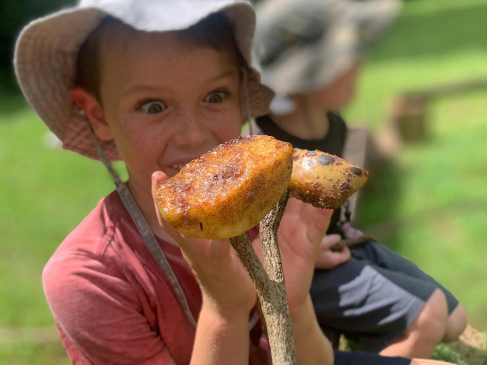 Child holding toasted fruit on stick at Birdwings Forest School Kids Holiday Nature Adventures Gold
