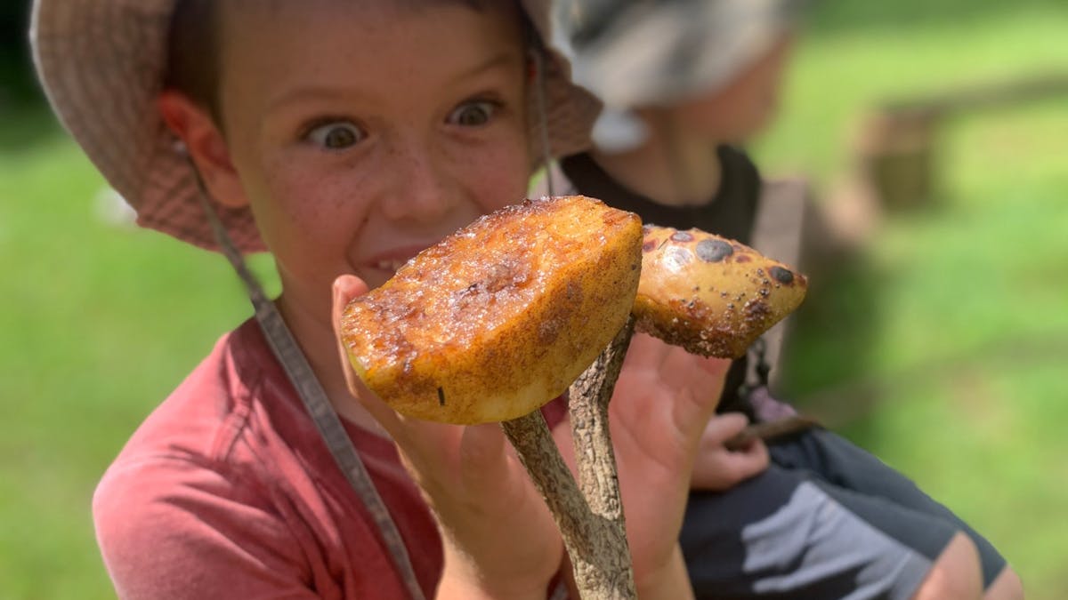 Child holding toasted fruit on stick at Birdwings Forest School Family Campfire Cookout