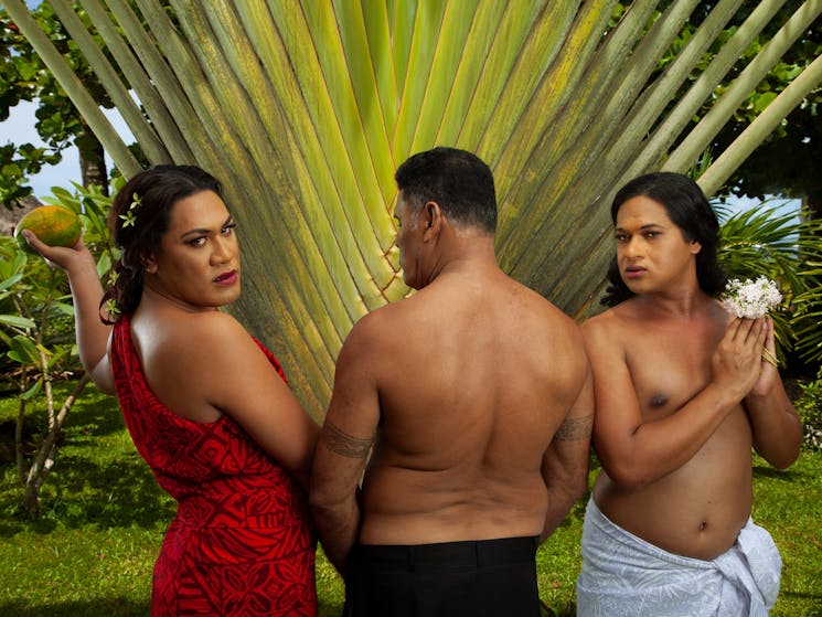 Three Fa'afafine, two facing the camera and the one in the middle facing the lush jungle