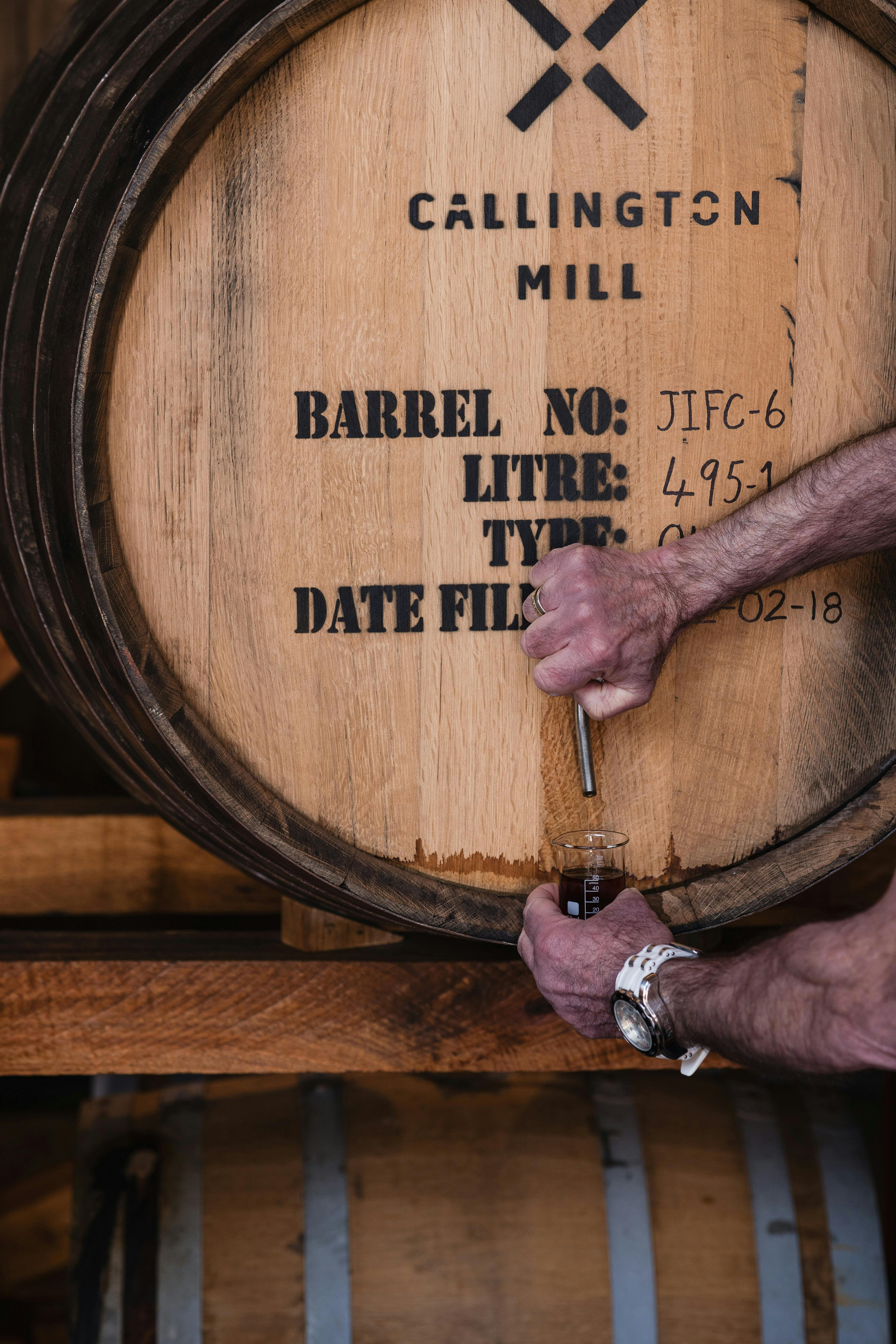 Two hands opening a tap on a whisky cask