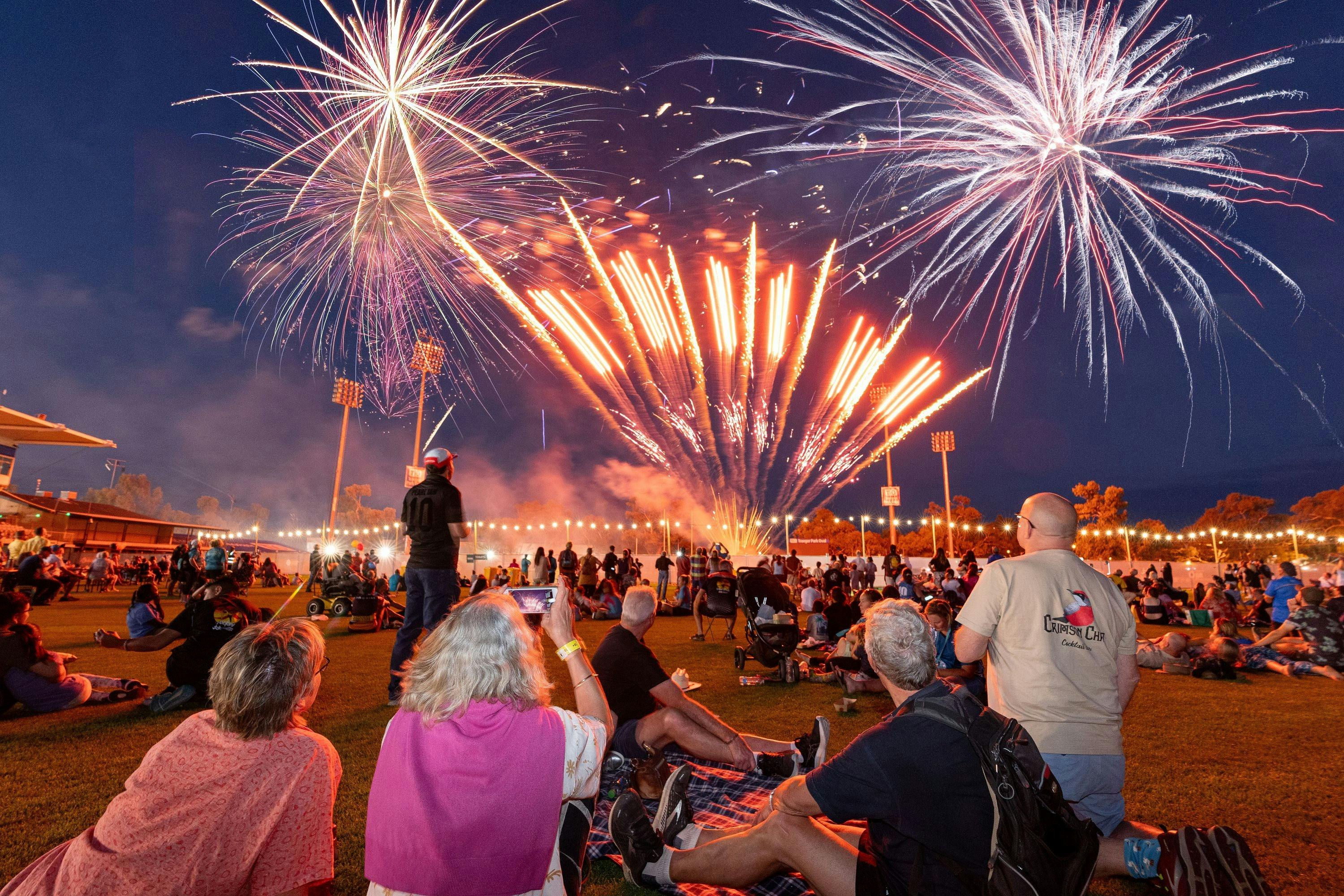 Fireworks in the sky at opening ceremony as groups of people watch on