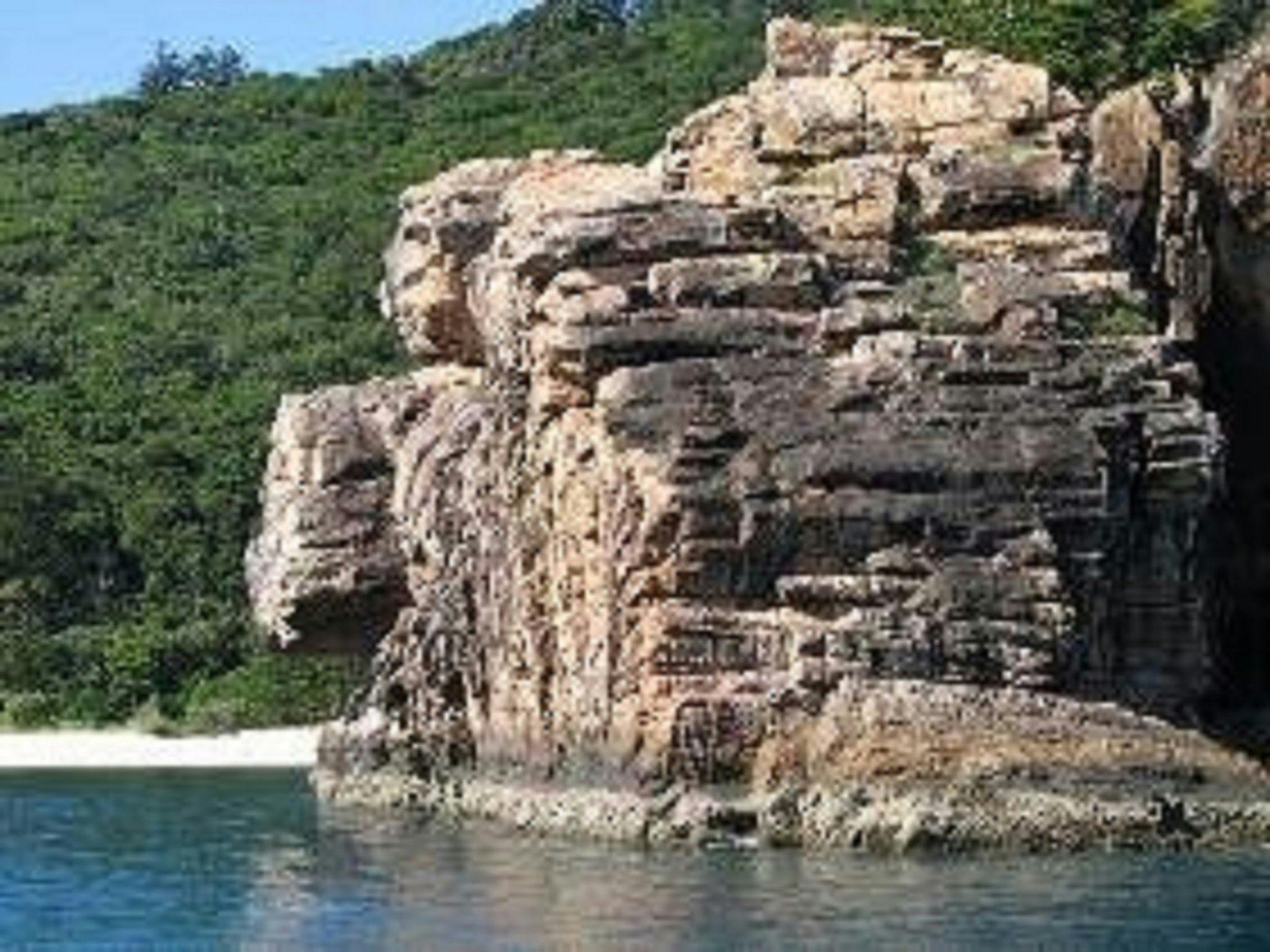 View to a large cliff reaching into the ocean with small beach in the background View to a large cliff reaching into the ocean with small beach in the background