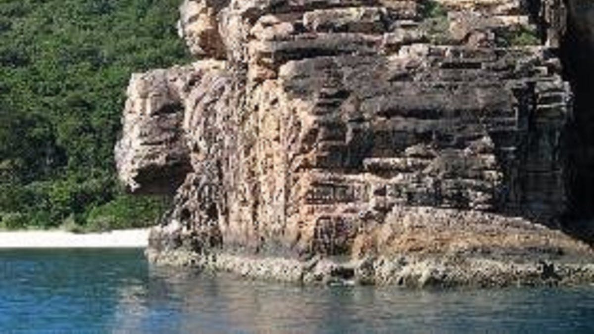 View to a large cliff reaching into the ocean with small beach in the background