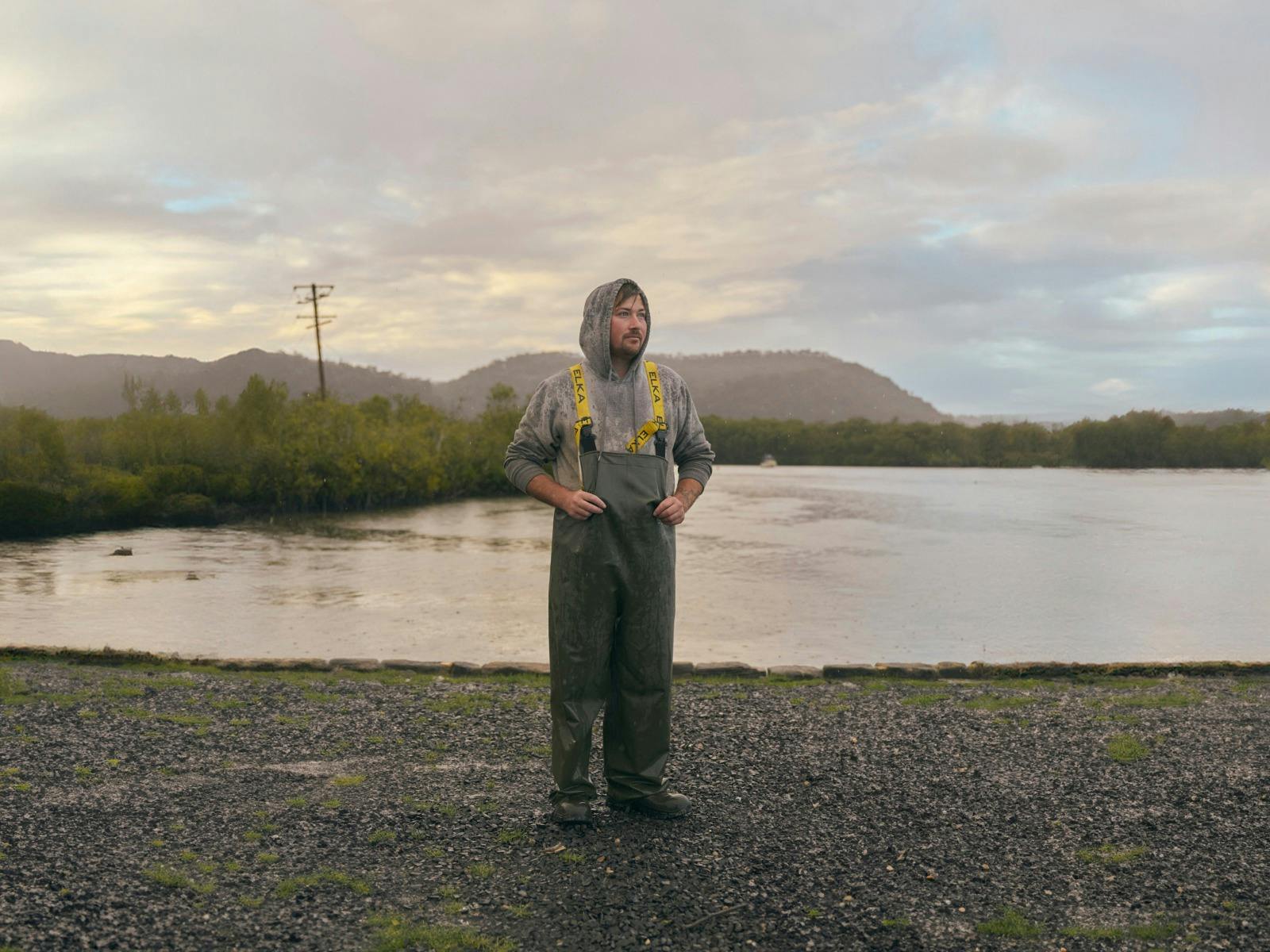 Man in hoodie and overalls standing in front of Hawkesbury River