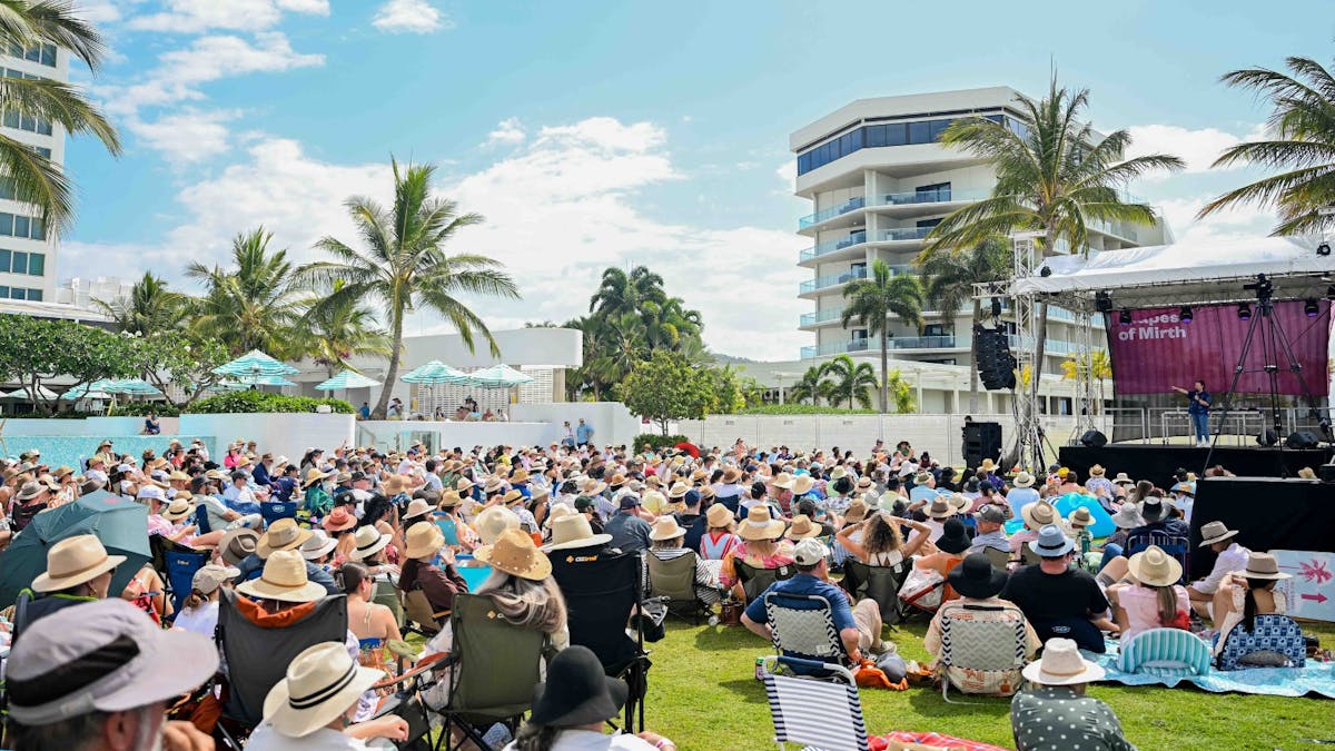 Large crowd seated on the grass watching an outdoor comedy show in Townsville.