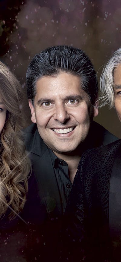 Four people in dark clothing smiling at the camera against a dark, shimmery backdrop
