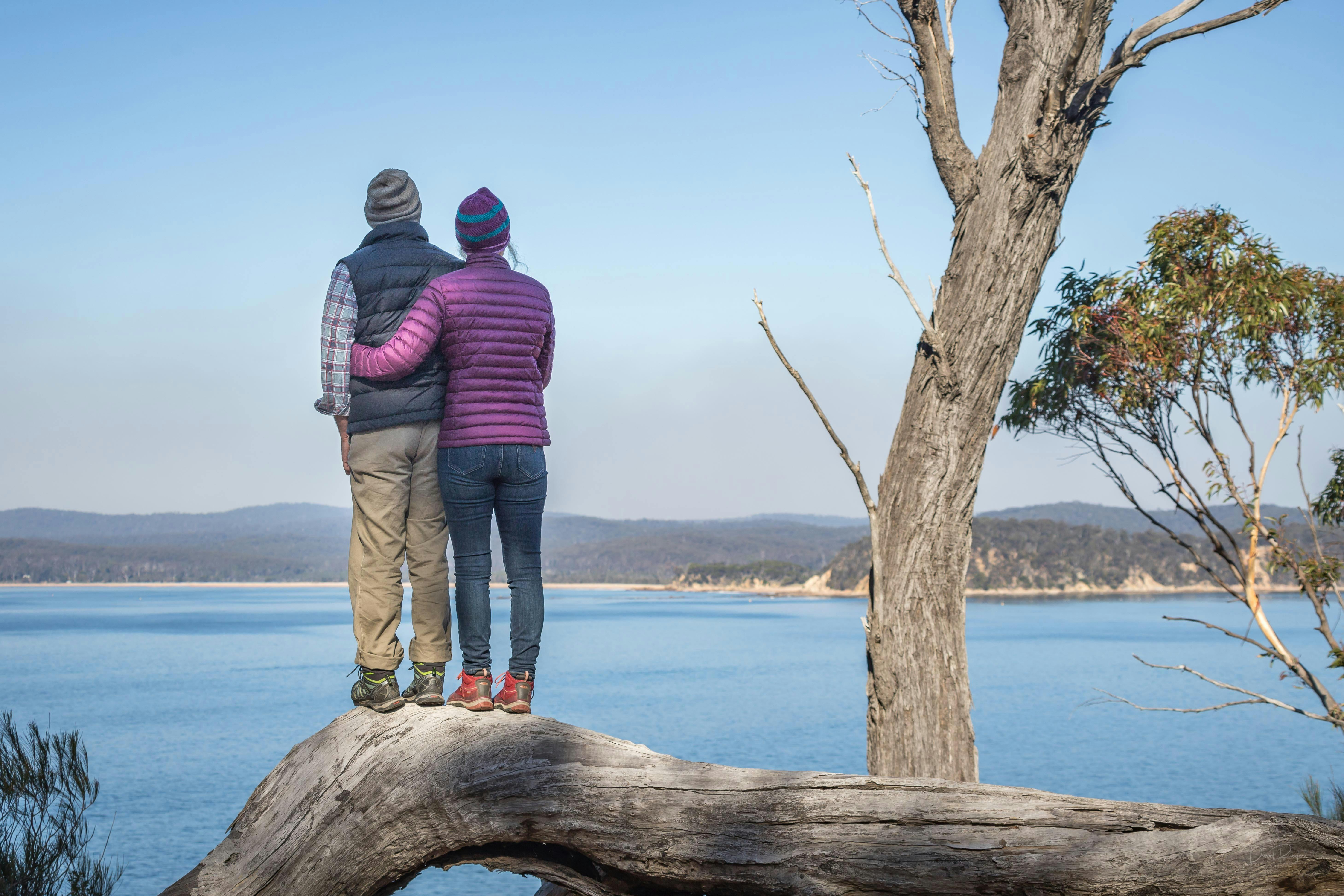 Couple in warm clothes standing on rock looking out to sea