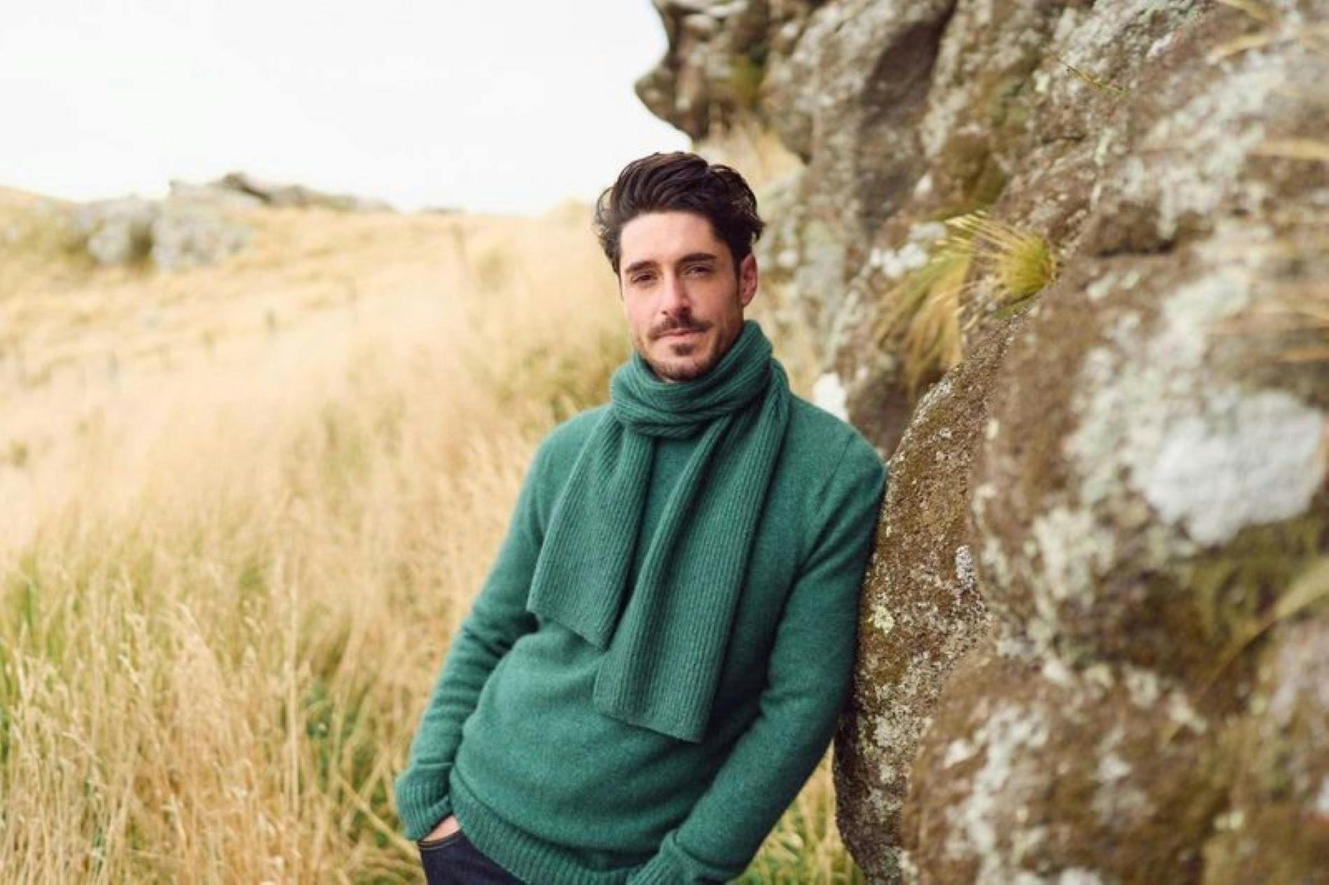 Man Leaning against rock in a grass field wearing Merinomink sweater
