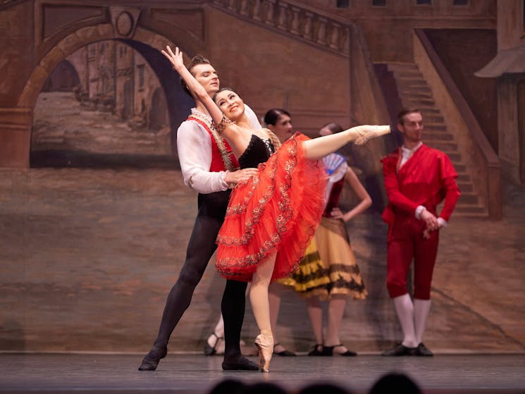 Woman in red dress and ballet shoes dancing with man wearing a white top and black pants