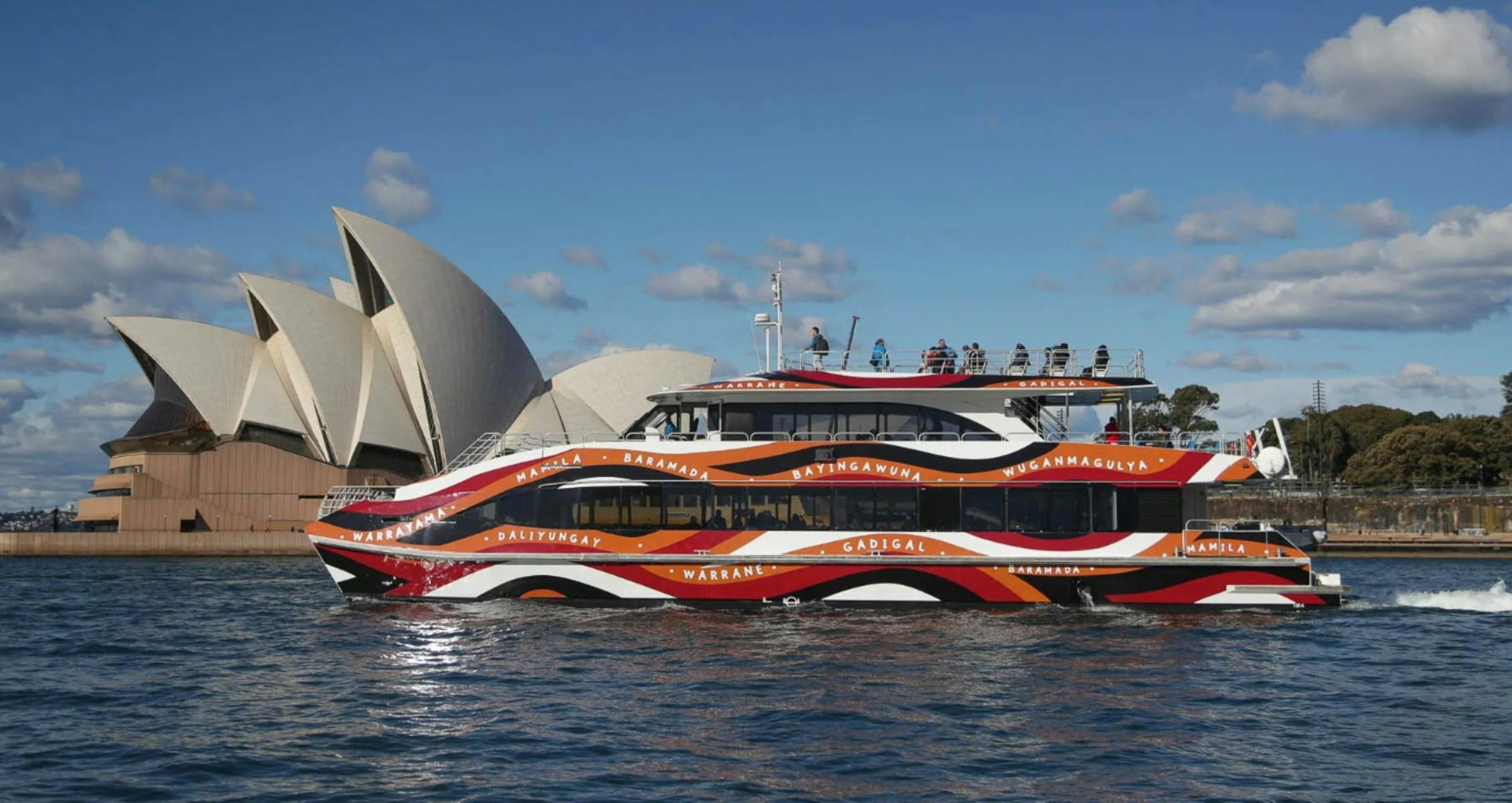 A vibrant ferry with Aboriginal art sails in Sydney Harbour, with the iconic Sydney Opera House in t