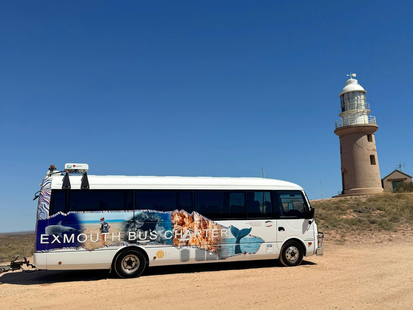 Exmouth Bus Charter bus in front of Vlamingh Head Lighthouse, ready for sightseeing tour.
