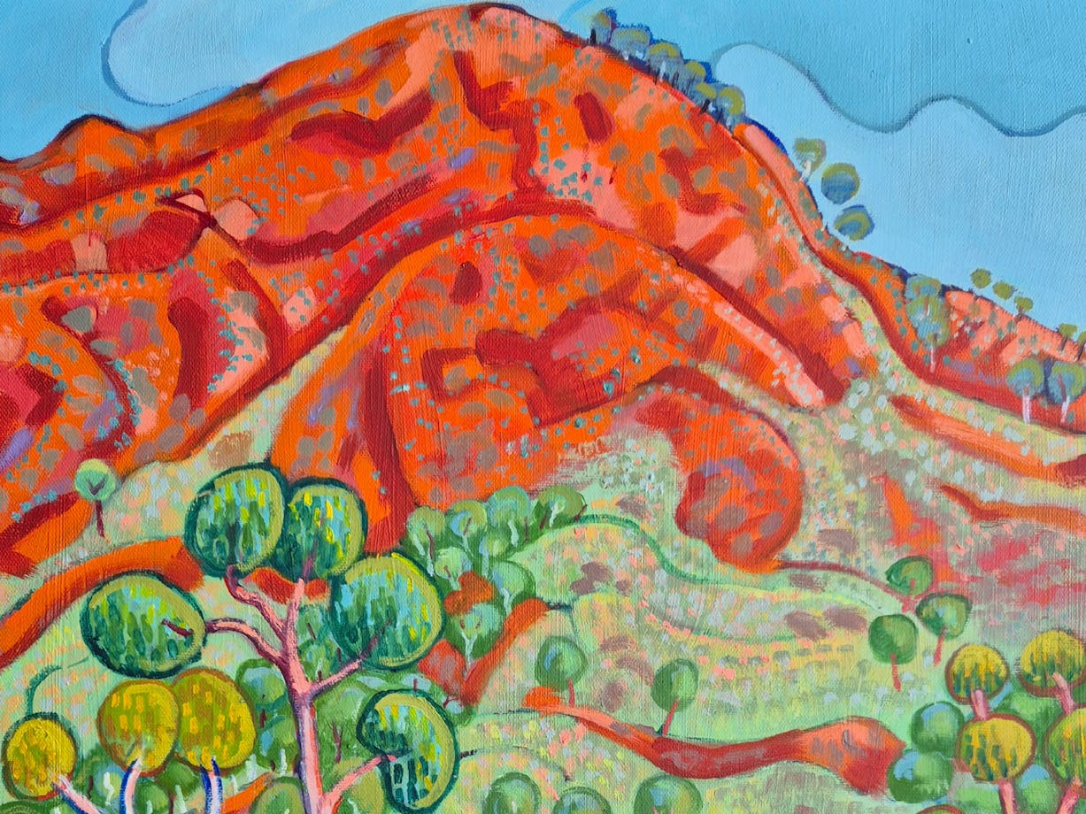 a bright orange hill with a blue sky and a green tree in the forground