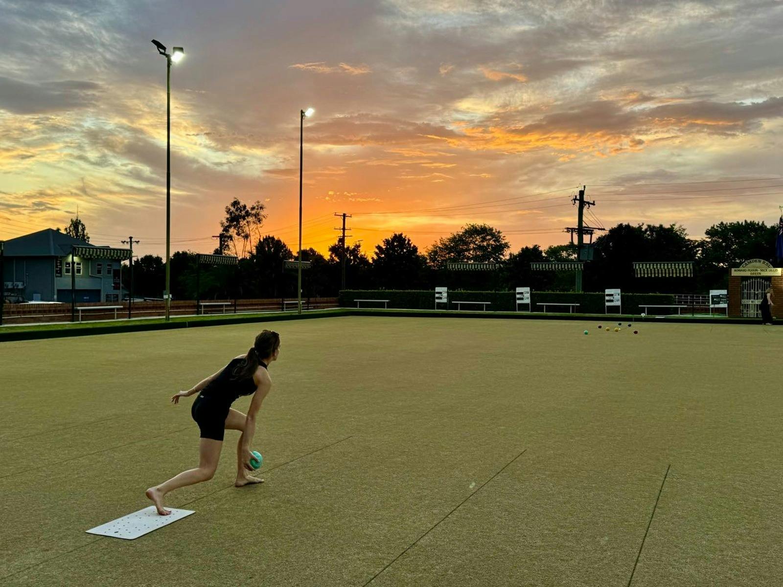 Girl on a bowling green at sunset bowling
