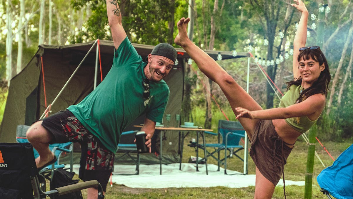 A male and femail doing a happy dance in fornt of thier tent which is all set up and ready to enjoy