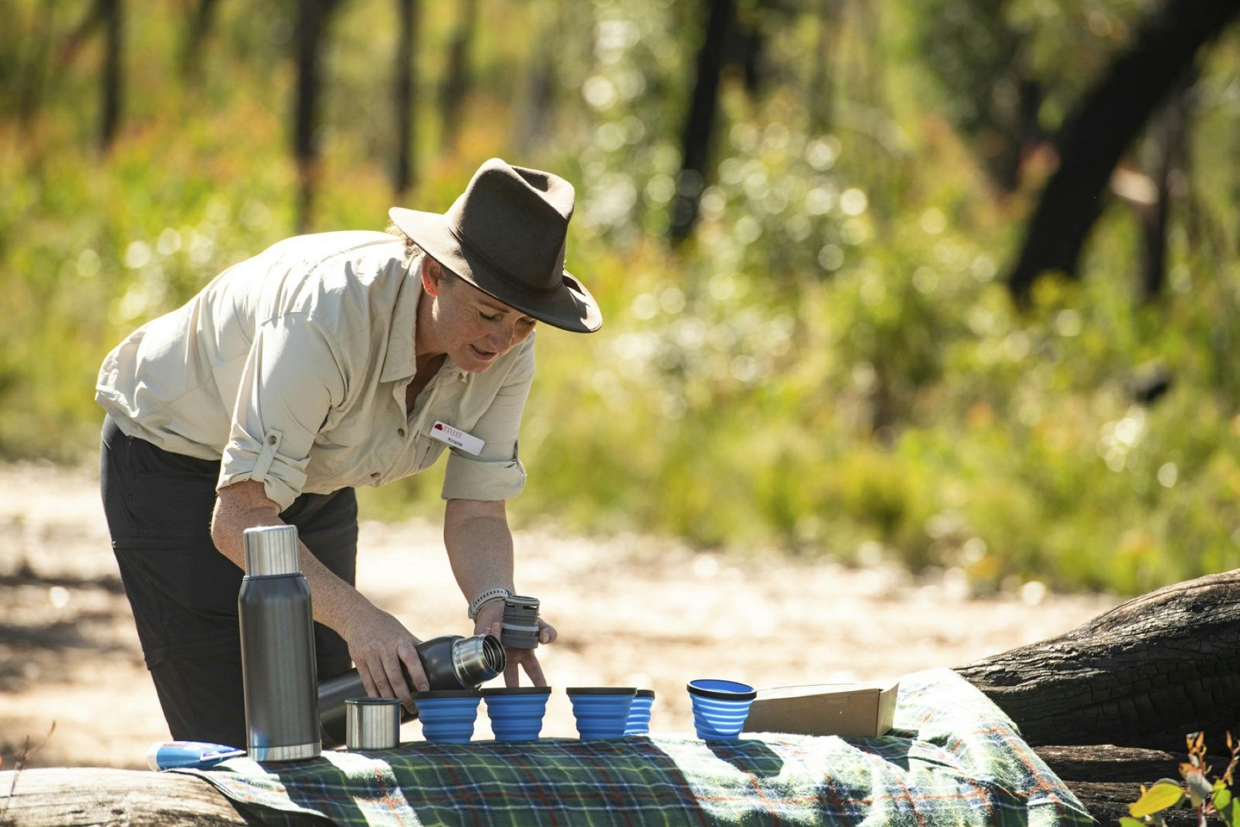 Our guide preparing morning tea pouring hot espresso coffee into blue mugs on a green picnic rug.