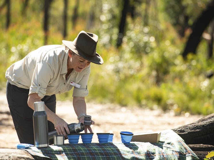 Our guide preparing morning tea pouring hot espresso coffee into blue mugs on a green picnic rug.
