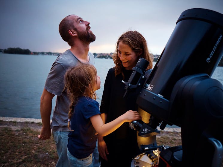 Woman, man and child looking at the stars next to a telescope