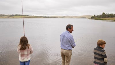 Young girl, adult male and boy standing on the edge of Pejar Dam