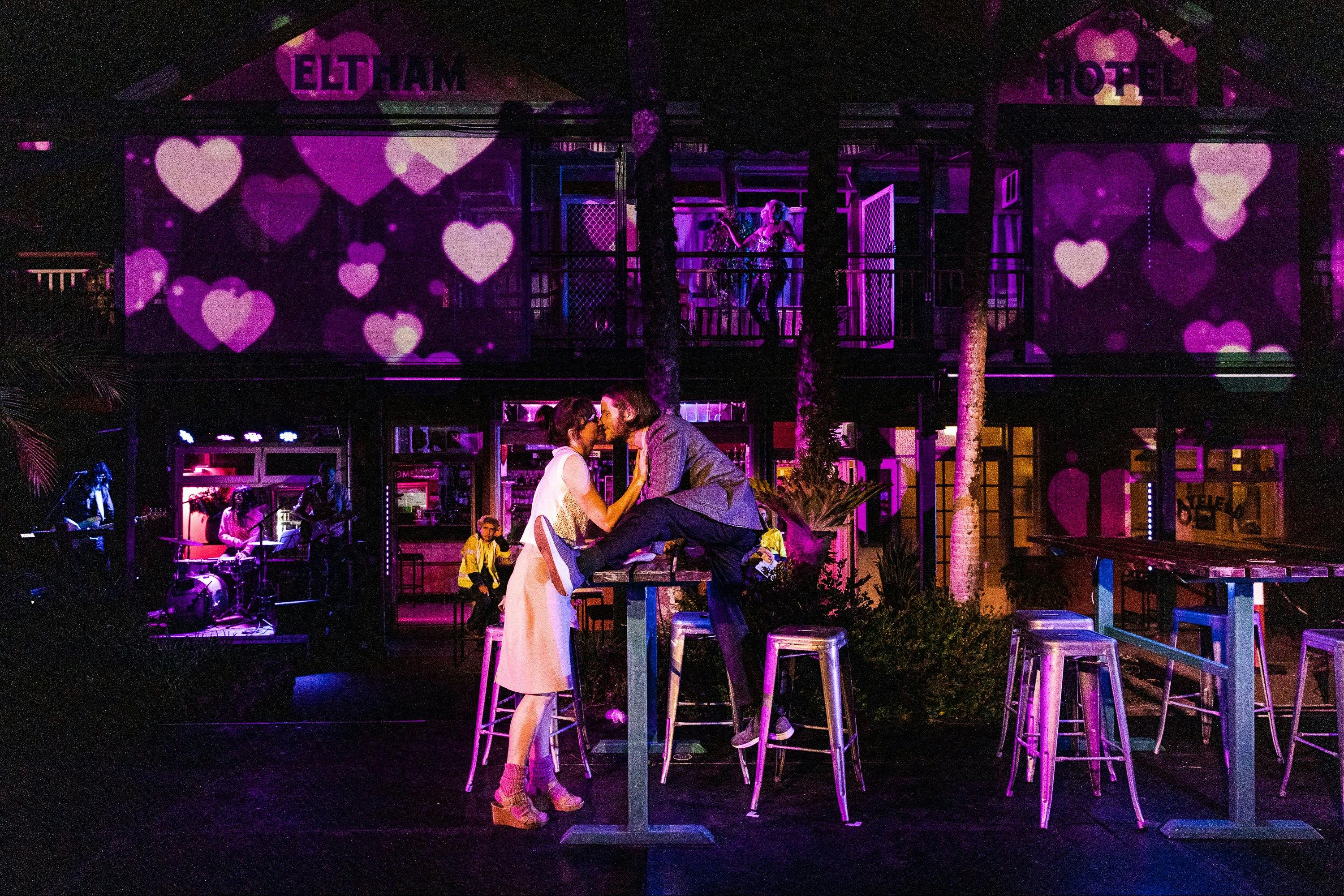 A couple embrace against the backdrop of  the Elthem Hotel