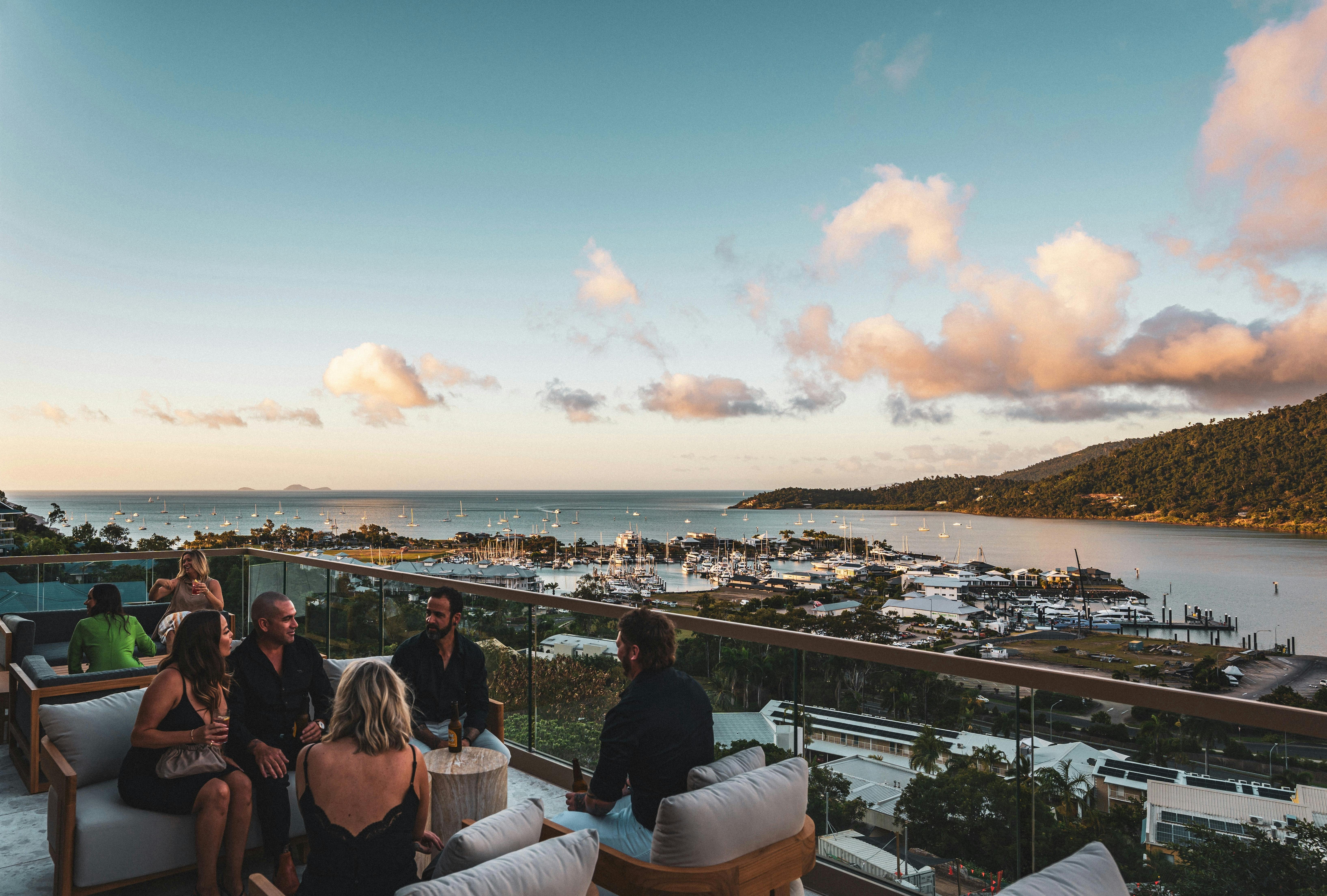 A group of people enjoy a drink on the rooftop bar with a backdrop of the Coral Sea
