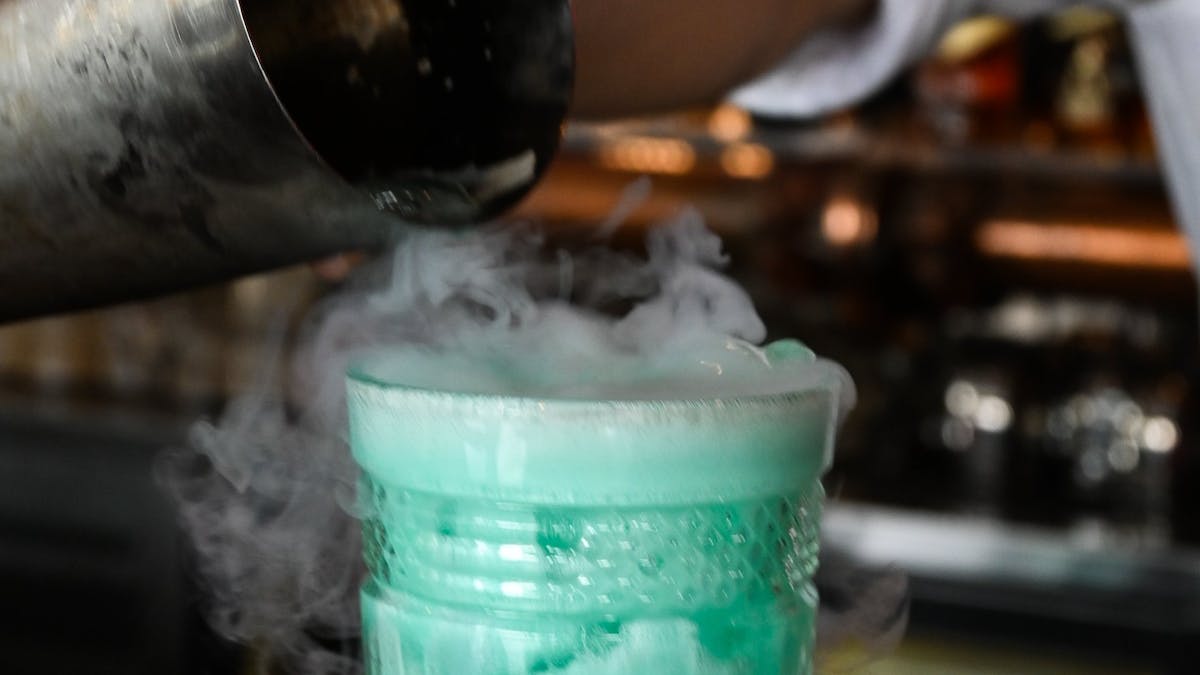 Blue cocktail being poured at bar with cold ice